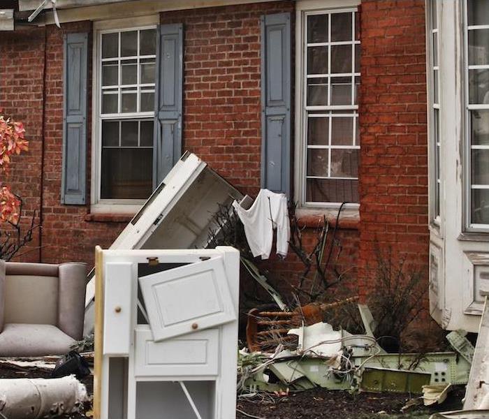 damaged furniture and other home items sitting outside of red brick house ” >
