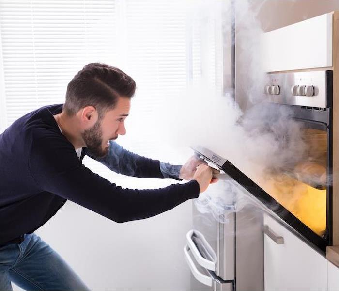 a man with blue shirt opening oven filled with smoke